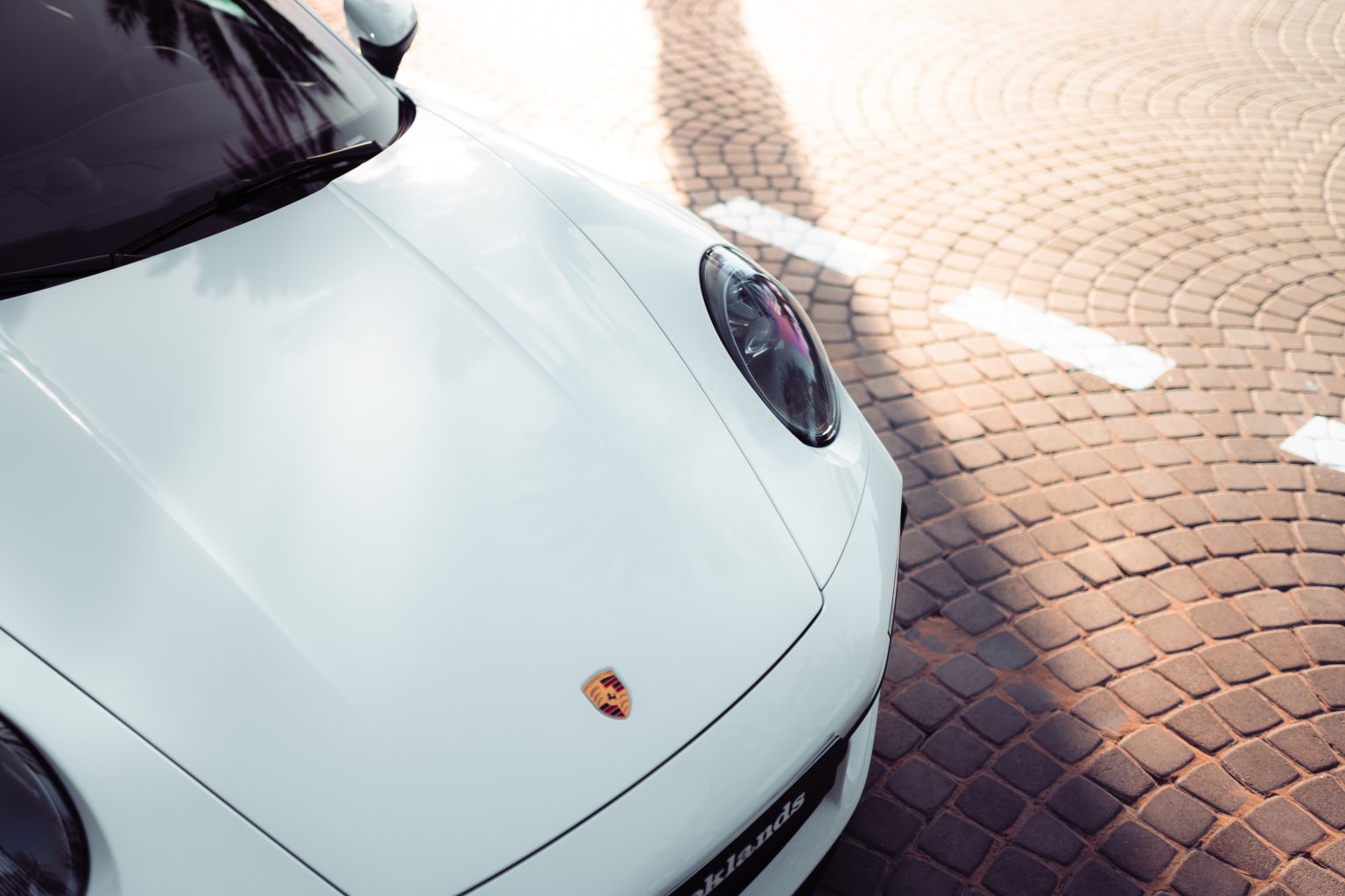 Close-up of a white Porsche 911 hood and headlight outdoors, part of the Brook Drive fleet