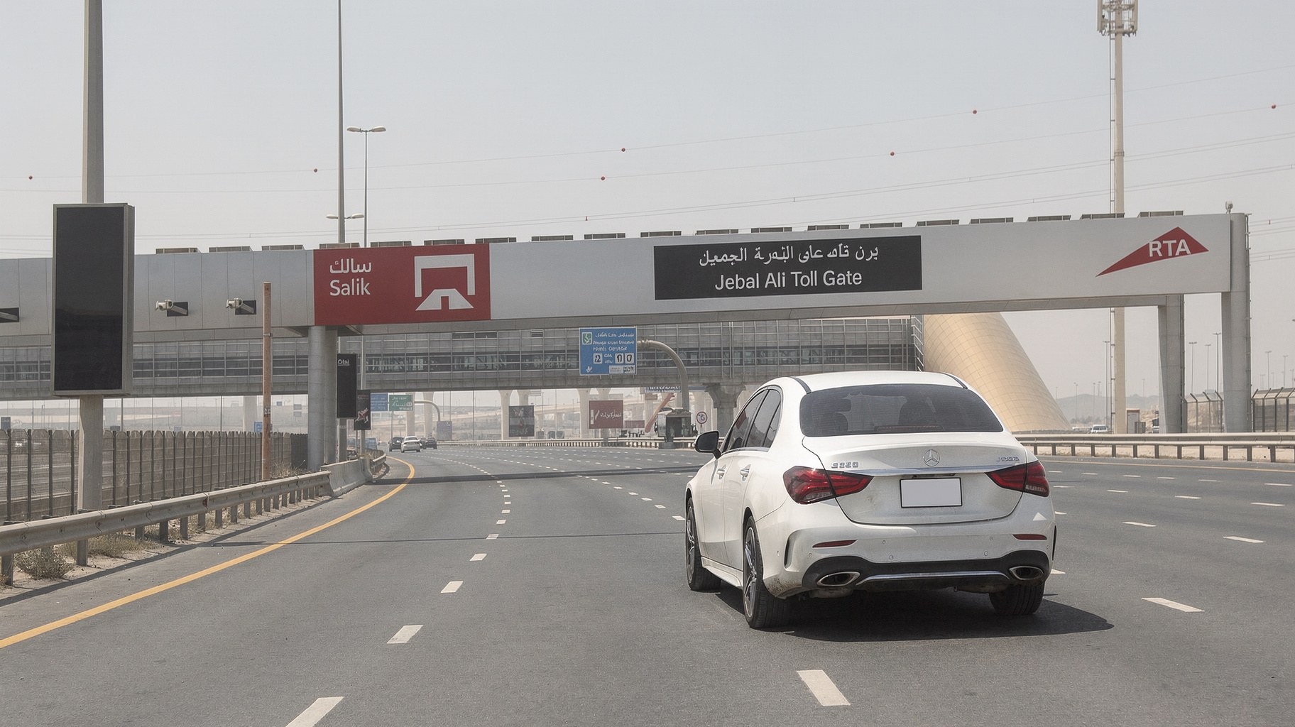 White Mercedes C200 passing under a Salik toll gantry on Sheikh Zayed Road in Dubai