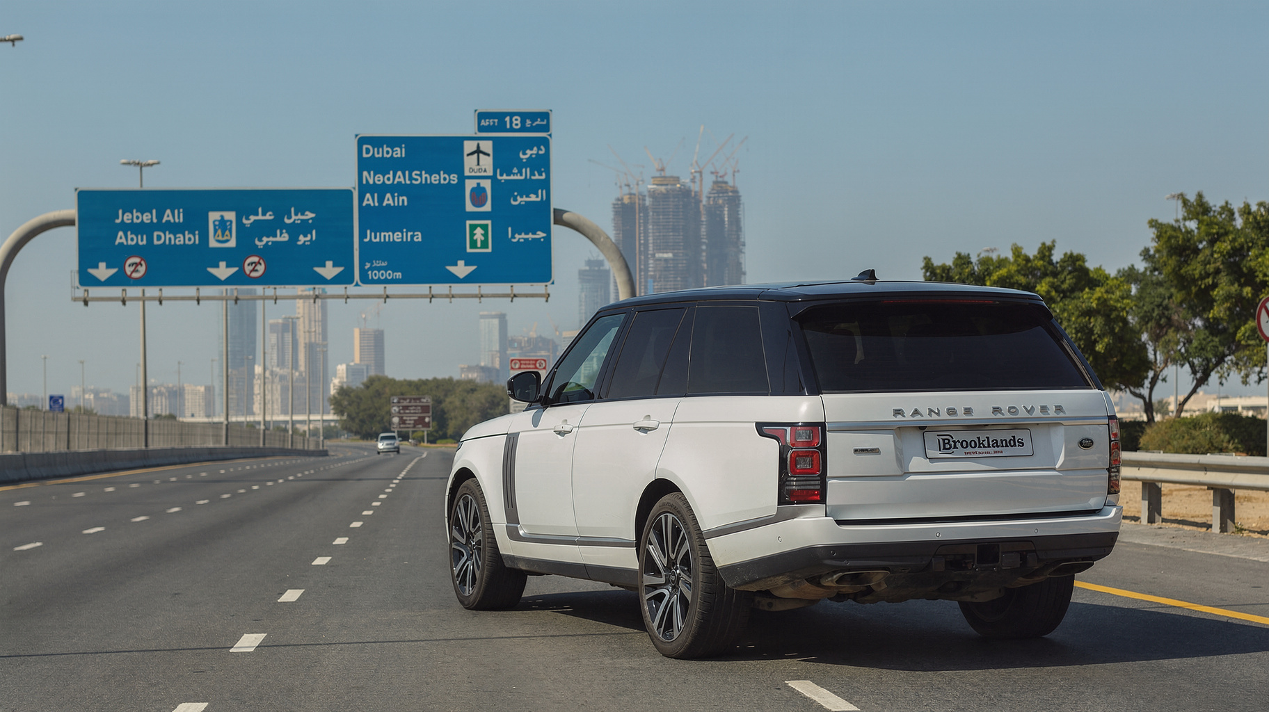 White Range Rover driving beneath overhead Dubai and Abu Dhabi highway direction signs