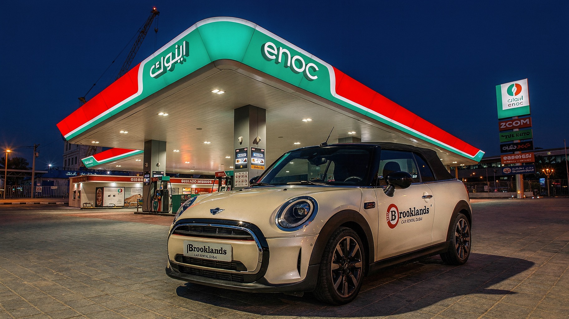 Mini Cooper S Convertible blanco de la flota de Brook Drive aparcado en una gasolinera de Dubái al atardecer